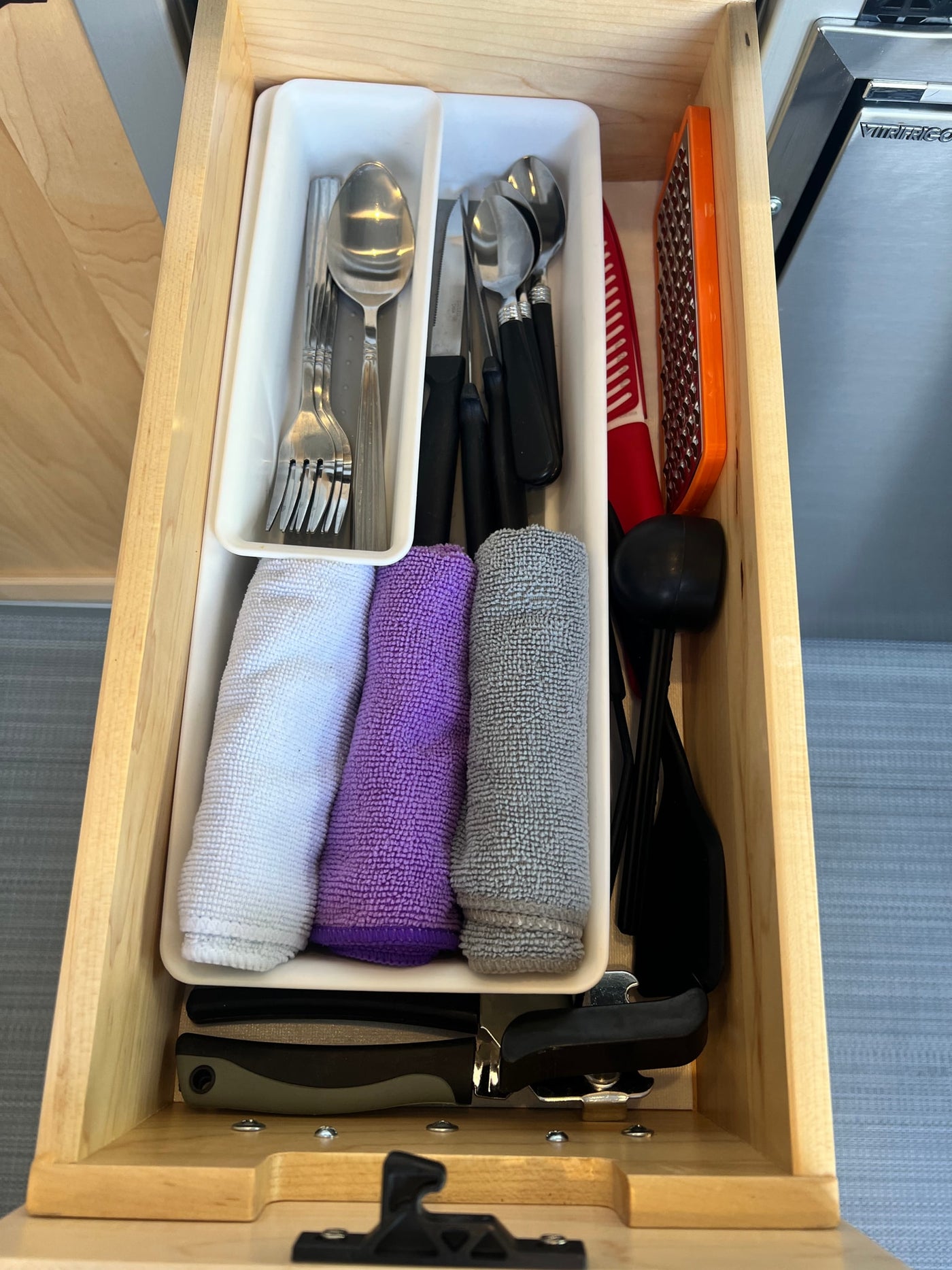 Organized RV rental kitchen drawer with silverware, knives, microfiber towels, grater, and various cooking tools. — photo 13