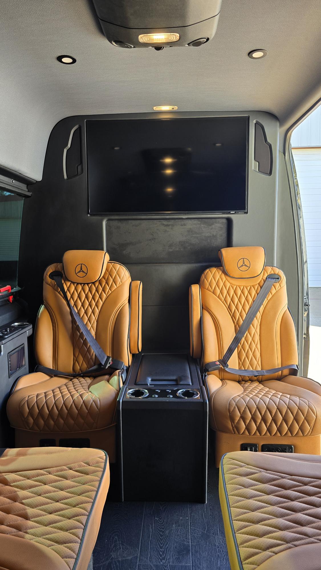 Step inside this RV rental! Plush tan leather captain's chairs with Mercedes-Benz logos, a large TV, and a central console create a luxurious interior.