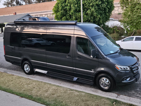 A dark gray Mercedes-Benz Sprinter camper van, available for rv rental, parked on a residential street.