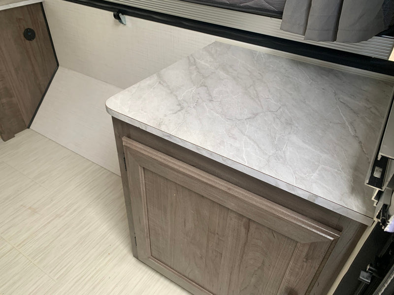 RV rental interior: A modern cabinet with a marble-look countertop, light wood door, and textured floor in a compact camper. — photo 8