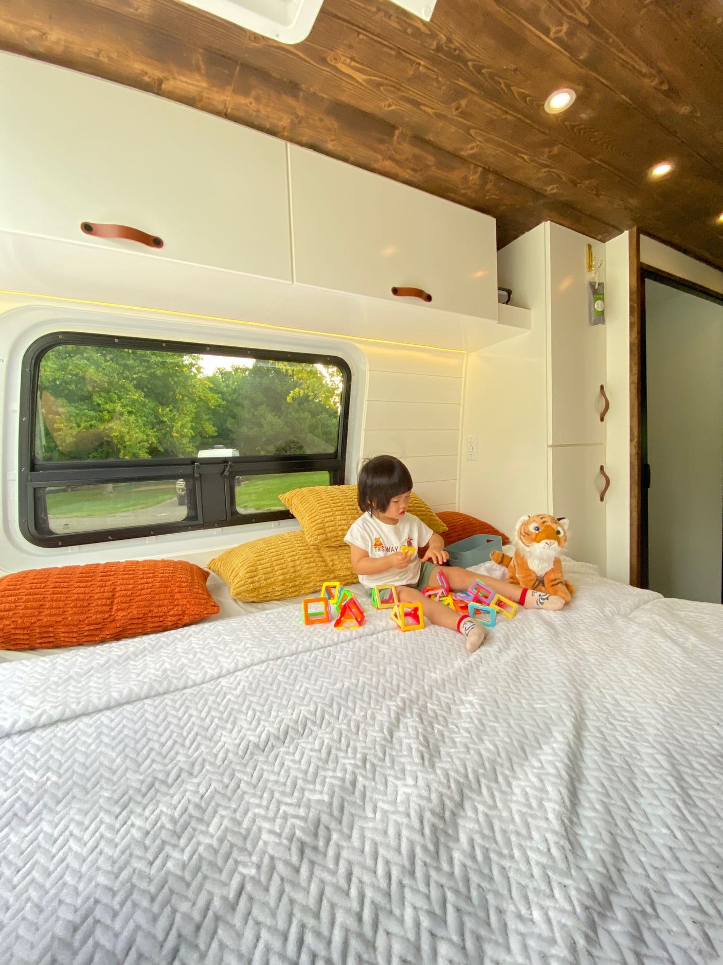 Child enjoying playtime in a cozy RV rental bed. Bright interior, wooden ceiling, and nature view.