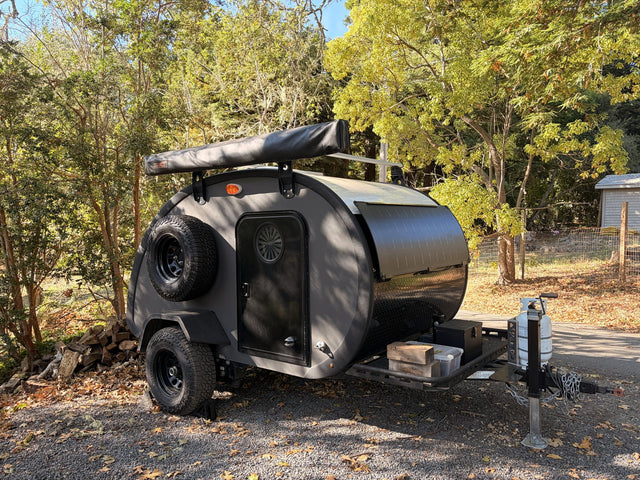 2022 Bean Meaner Bean teardrop camper, dark grey, front three-quarter exterior with roof rack and spare tire