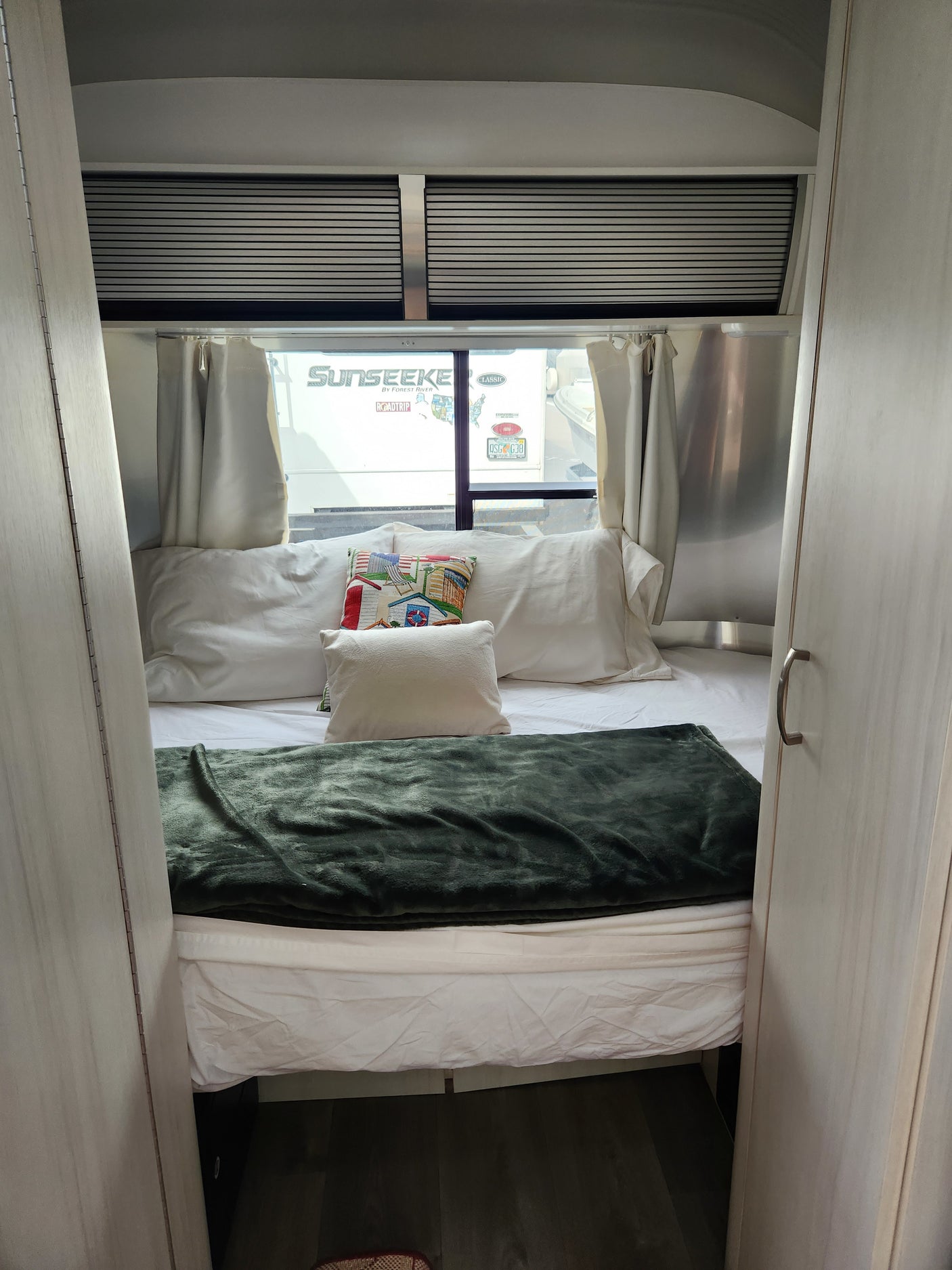 Comfortable RV rental bedroom: bed with a green blanket, pillows, and window view of another RV.