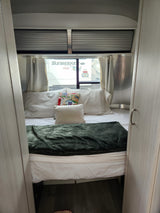 Comfortable RV rental bedroom: bed with a green blanket, pillows, and window view of another RV.