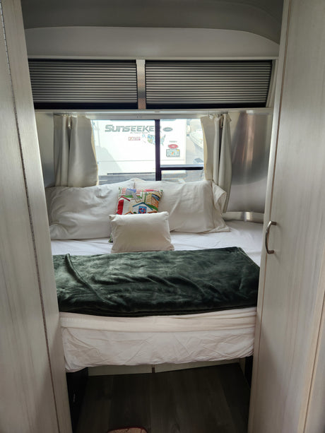 Comfortable RV rental bedroom: bed with a green blanket, pillows, and window view of another RV.