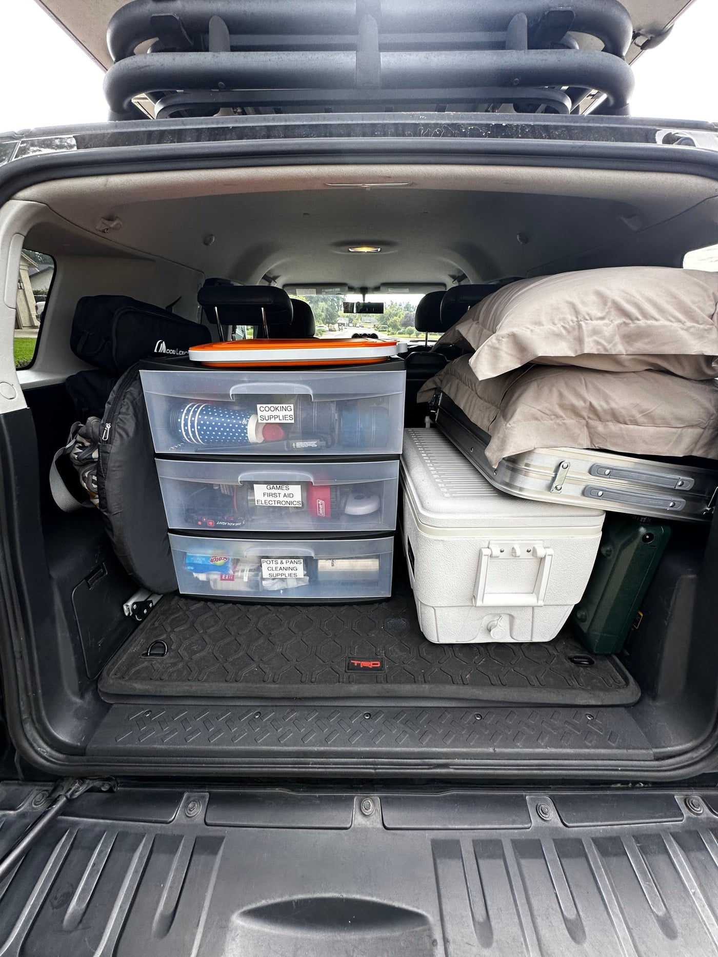 RV rental ready: SUV cargo packed. Labeled bins for cooking, first aid, games, cleaning, plus cooler & table visible. — photo 13