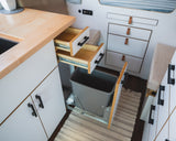 An RV rental's clever kitchen design: light wood counters, open drawers, and a pull-out trash bin for efficient use of space.