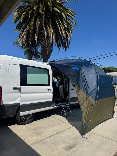 Sunny day with a white RV rental camper van and a dark blue/green Kelty screen room attached for outdoor shade.