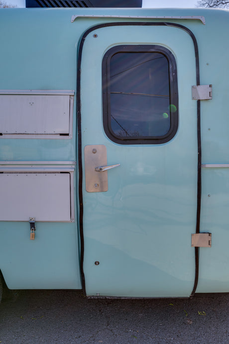 Light blue RV rental side showing the entry door with window, handle, and secured storage compartments.