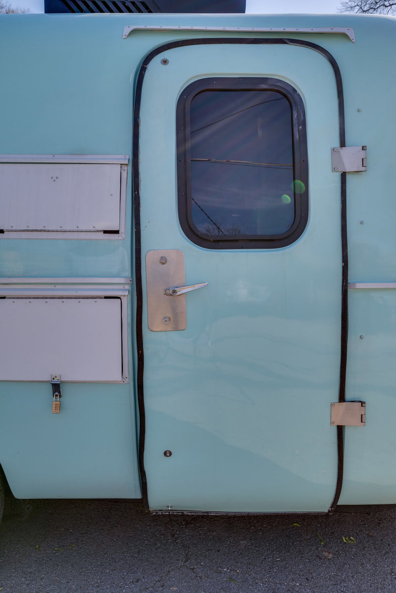Light blue RV rental side showing the entry door with window, handle, and secured storage compartments. — photo 12