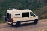 RV rental: A beige camper van parked on a road overlooking a vast green forest, equipped for adventure travel.