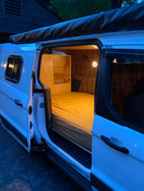 Step inside this charming white camper van conversion, ideal for an RV rental. Features a custom plaid interior and comfy bed.