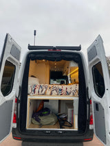 View an rv rental camper van's open rear, revealing a comfy bed, cozy interior lighting, and organized storage for travel.
