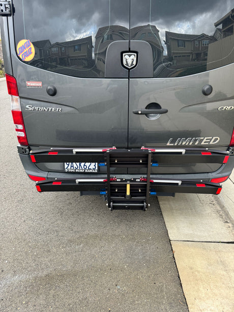 Rear view of a gray Sprinter van, typical for an rv rental, equipped with a mobility device carrier. Parked on a street.