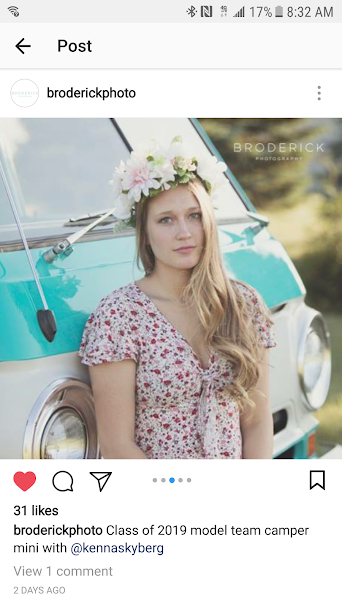 Young woman with flower crown poses in a floral dress beside a teal vintage RV rental. A senior model photoshoot.