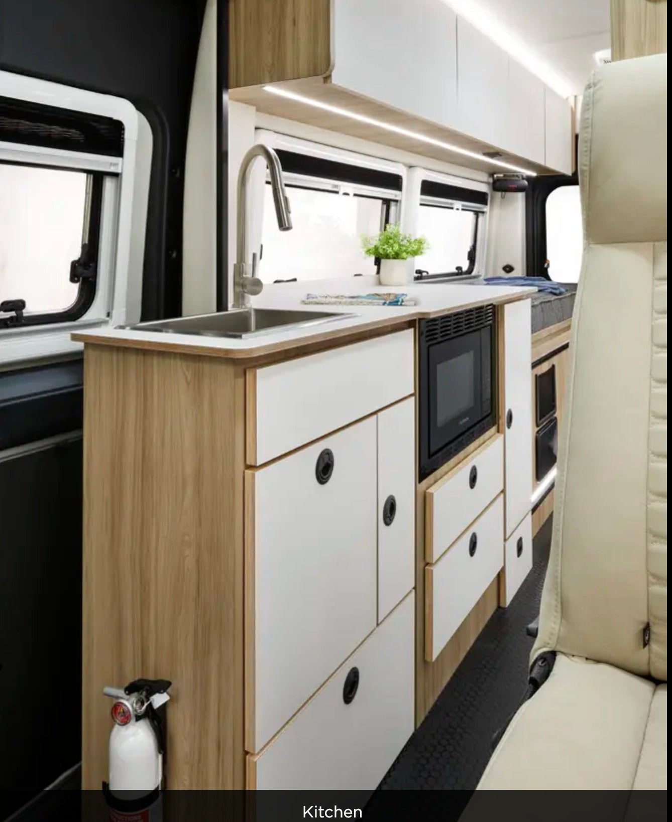 Interior of an RV rental: compact kitchen with a sink, microwave, and storage cabinets for convenience.