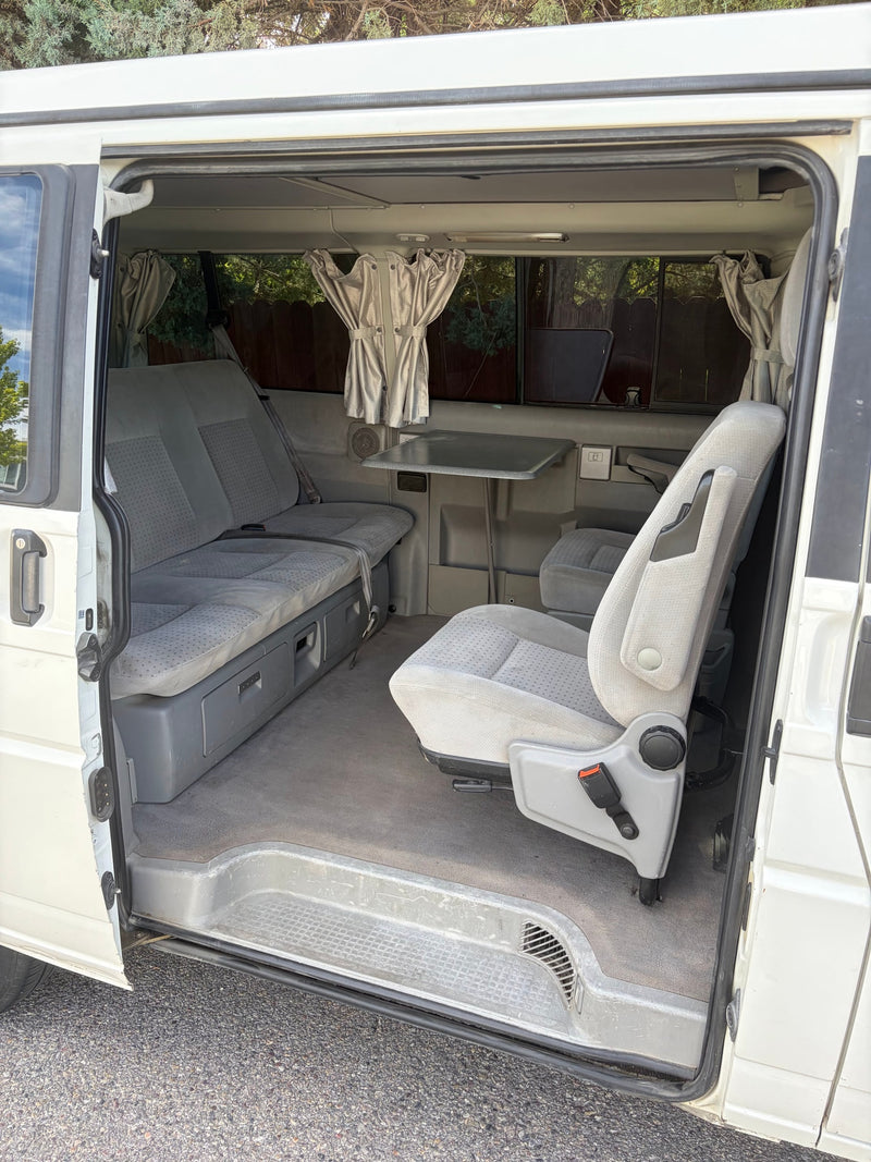 RV rental camper van interior. Features a rear bench, swivel passenger seat, and fold-out table, ideal for travel and camping. — photo 7