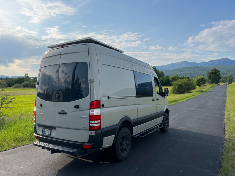 Light-colored camper van, equipped with solar, parked on a rural road with mountains & sky. Ideal for rv rental adventures. — photo 6