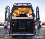 Explore this spacious rv rental camper van's rear view. Inside, find a comfy bed, wood-paneled ceiling with lights, & versatile storage.