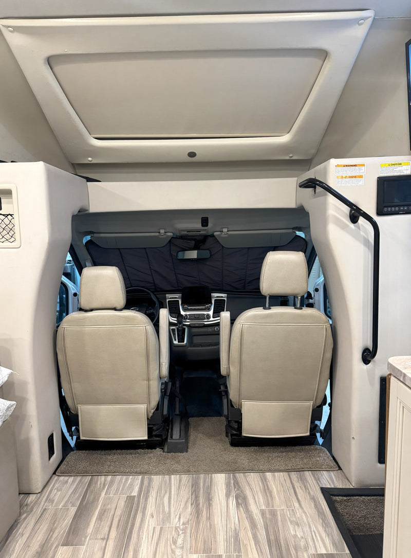 Interior view of an RV rental, showing the cockpit with two tan seats, dashboard, and an overhead bunk/storage area. — photo 9