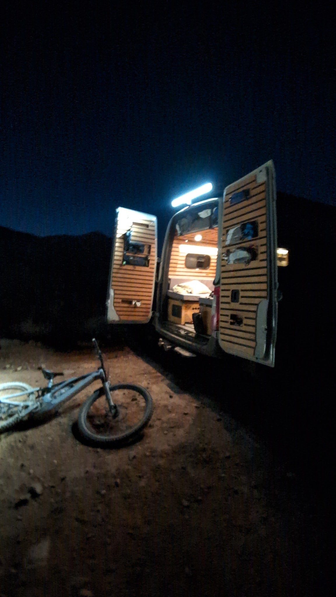 Night camping in an RV rental van with open doors, revealing a cozy interior, and a mountain bike on the ground. — photo 10