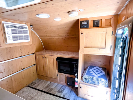 Inside this cozy rv rental, wood paneling, an AC unit, microwave, and storage create a comfortable space for travel.