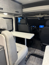 RV rental interior view: dinette with table, light gray seating, overhead cabinets, and driver's cab.