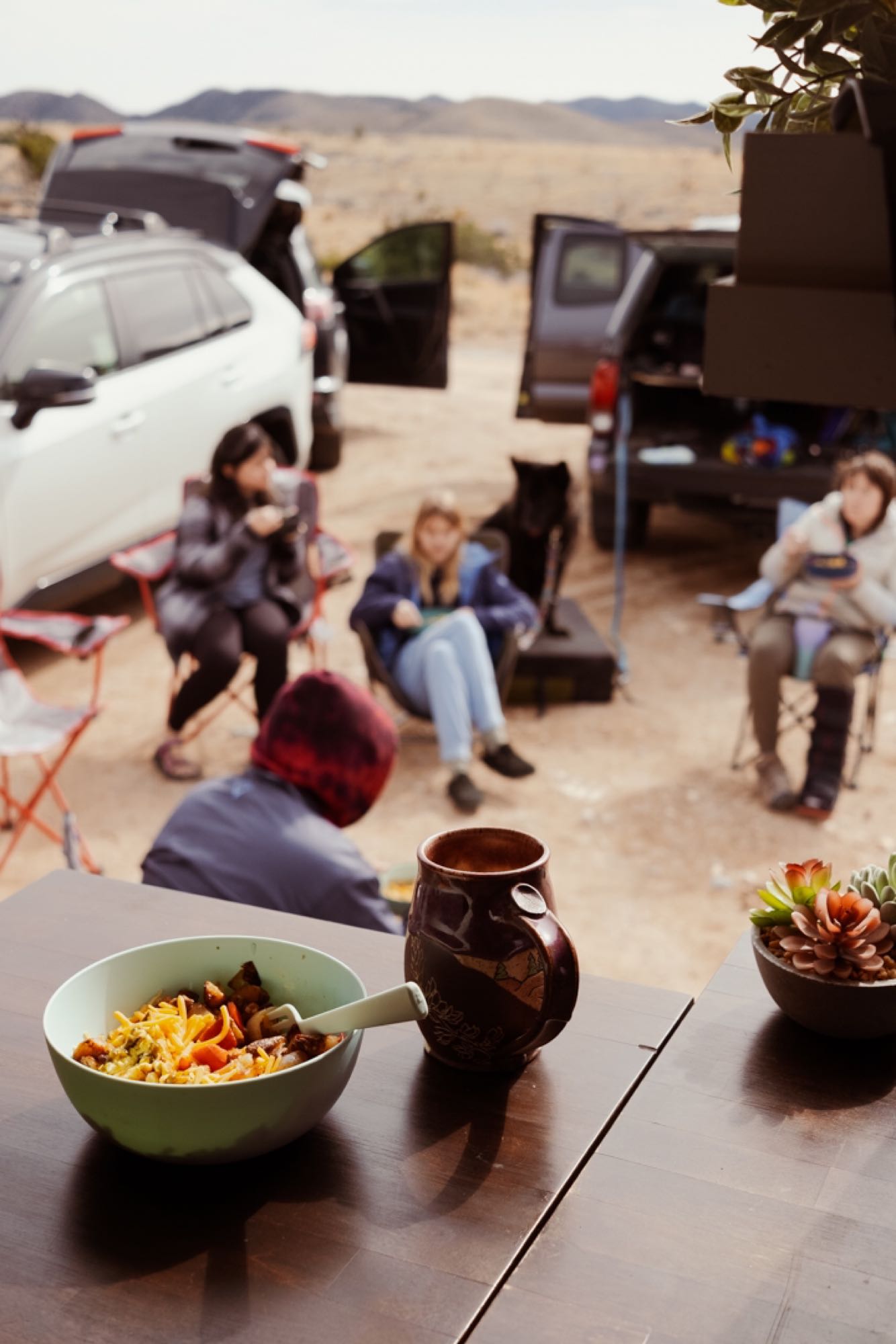Scenic RV rental camp in the desert. Friends gather while a bowl of food & mug sits on a table in the foreground. — photo 16