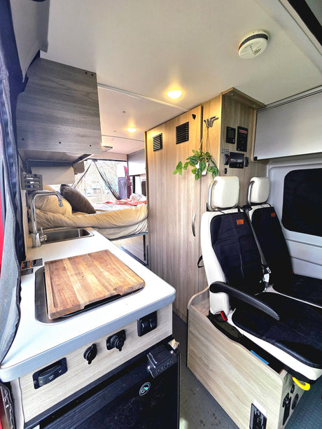 This RV rental features a well-equipped campervan interior with kitchen, bed, seating, and controls. Compact and ready for travel.