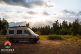Scenic RV rental adventure: a sleek camper van awaits amidst stunning mountains & glowing sunset. Ideal for outdoor exploration.