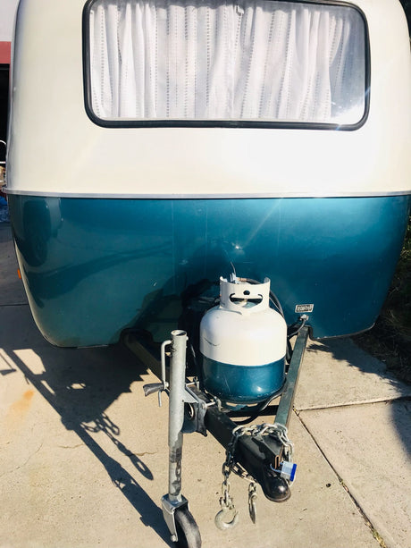 Teal & white travel trailer's front, with window, propane tank, and hitch, ready for your RV rental adventure.