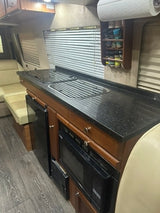 This RV rental's galley kitchen features black counters, a built-in stovetop/sink, microwave, and fridge, ideal for road trips.