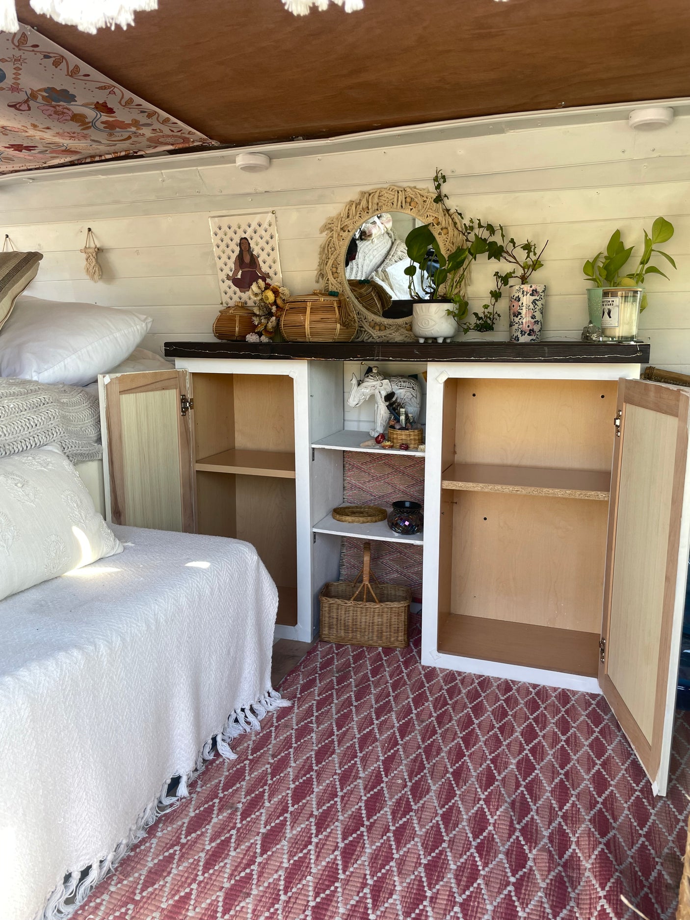 Bohemian RV rental interior featuring a daybed, open cabinets with decor, and a red geometric rug. Experience cozy travel.