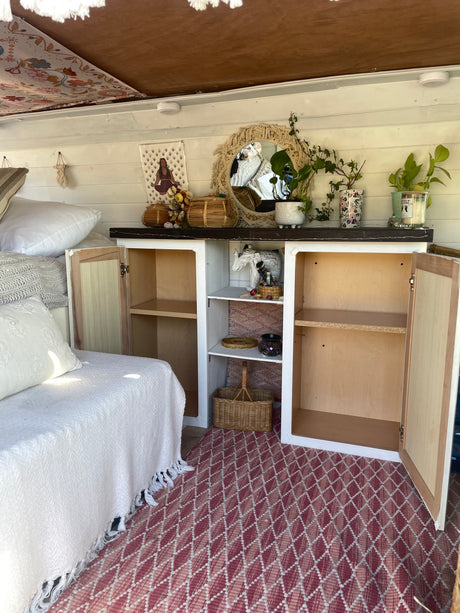Bohemian RV rental interior featuring a daybed, open cabinets with decor, and a red geometric rug. Experience cozy travel.