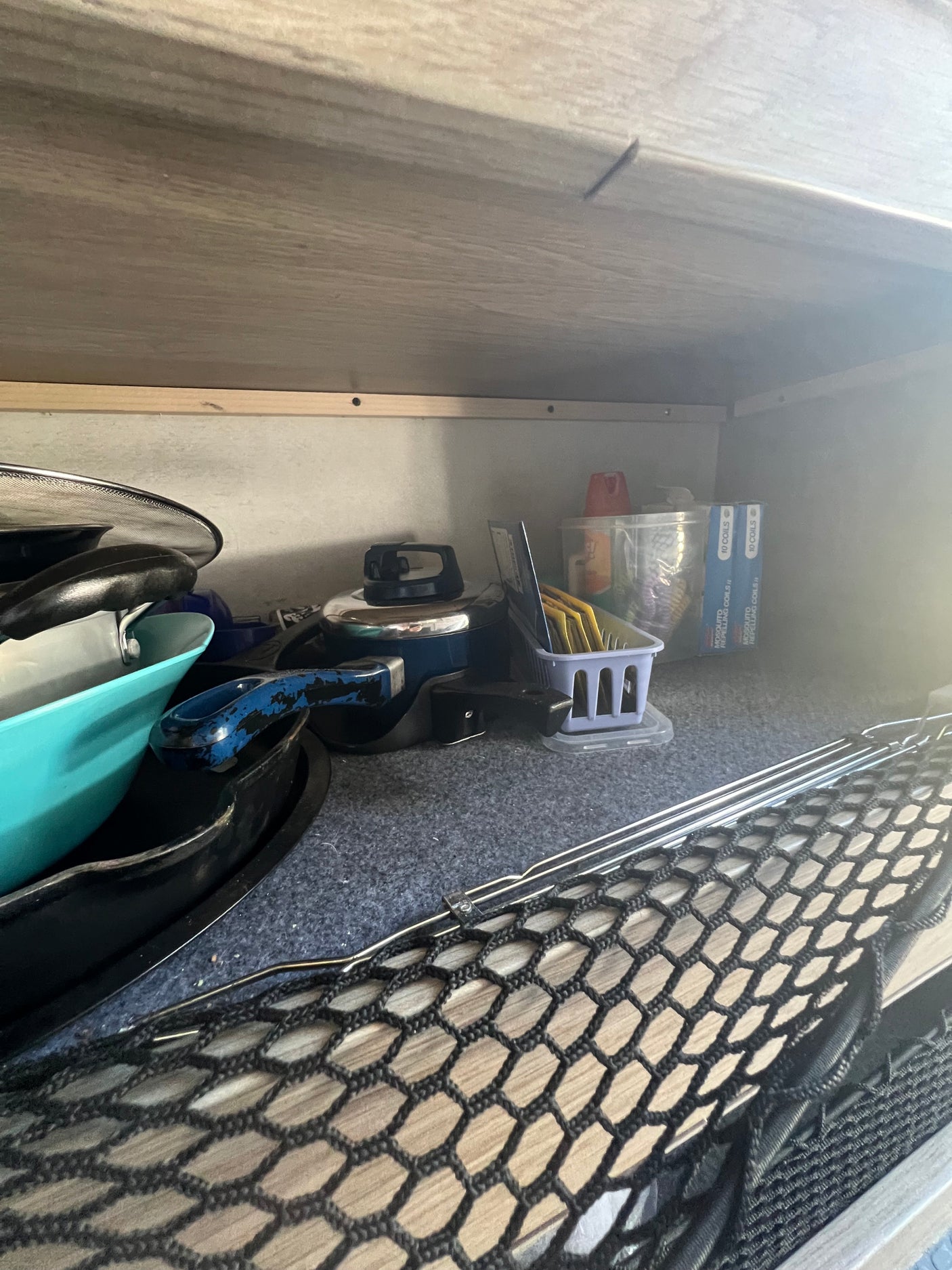 RV rental storage: A cabinet organized with cookware, cooking supplies, mosquito coils, and a securing mesh net.
