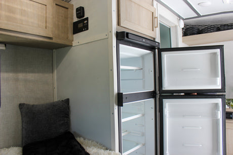 Empty fridge & freezer inside an RV rental, ready for your provisions. Features cabinets & control panel for an adventure.