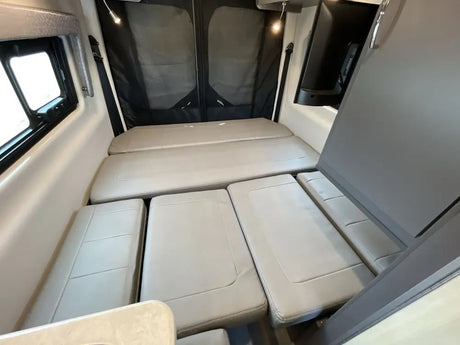 Inside an RV rental: light grey cushions form a bed in this cozy mobile living space. A window and TV are visible.