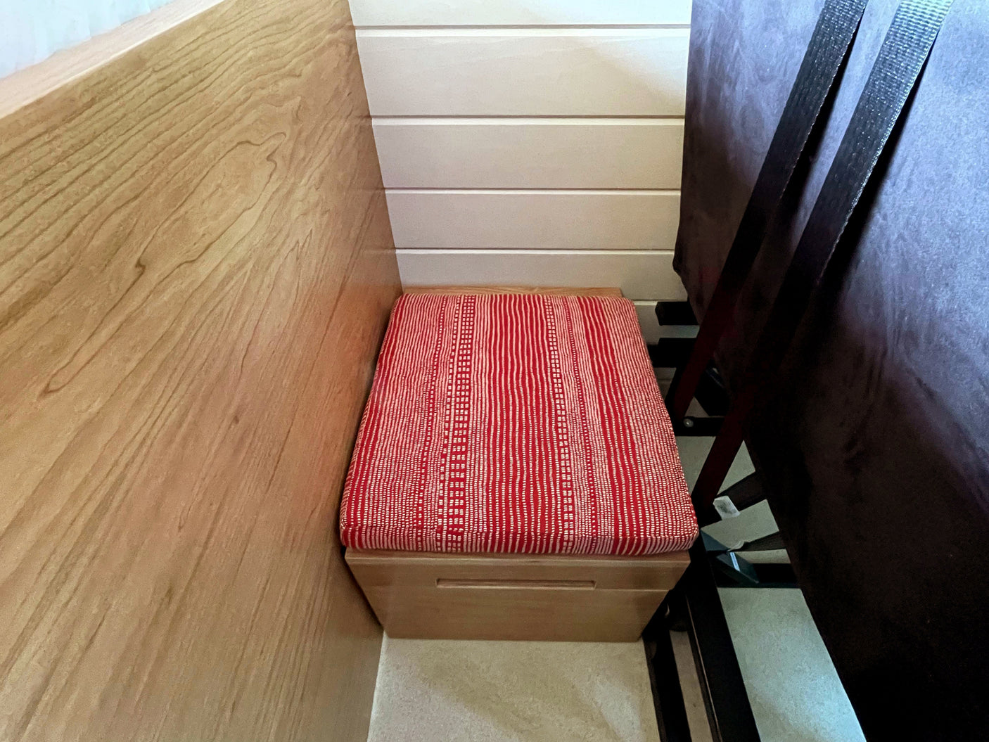 Red-cushioned bench and storage unit in an RV rental interior. Features wood and white paneled walls, with dark fabric to the right.