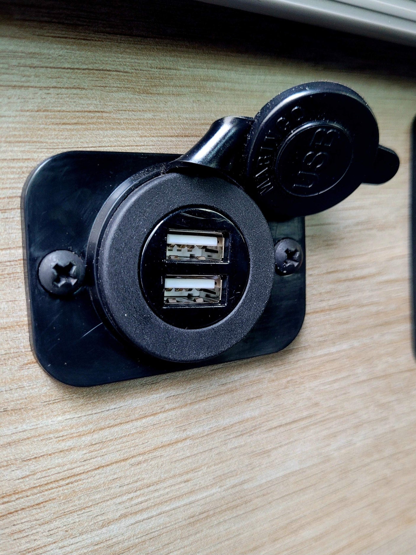 RV rental: Black dual USB charging port on light wood-grain paneling, cap open, ready to charge devices.