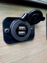 RV rental: Black dual USB charging port on light wood-grain paneling, cap open, ready to charge devices.