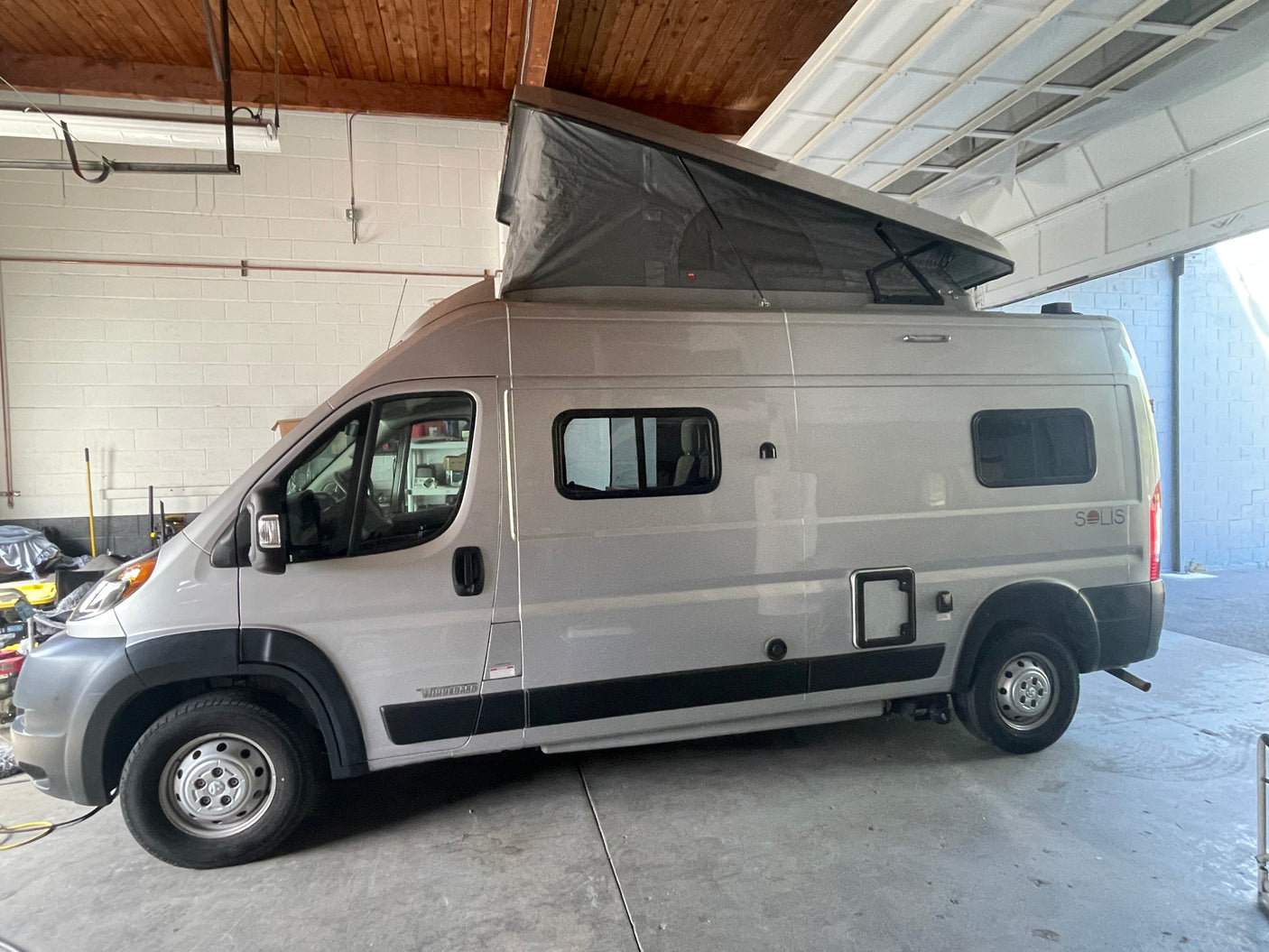 Light gray Winnebago Solis camper van with pop-top extended, parked indoors. Ready for your next RV rental adventure!