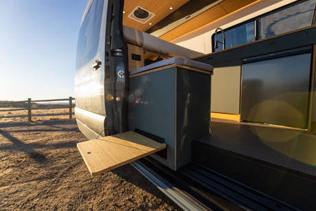 Modern **RV rental** camper van interior: kitchen with sink, fridge, and an outdoor pull-out bamboo table at the side door.