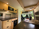 A spacious rv rental kitchen area, with wooden cabinetry, microwave, fridge, and view to the front cabin.