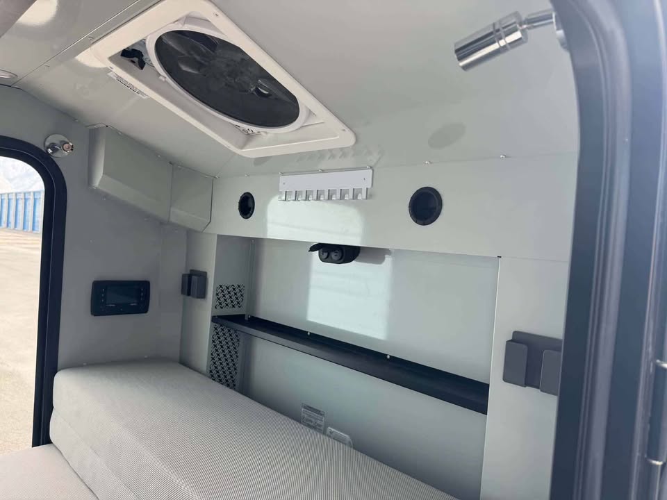 Interior cabin of the XPedition Voyager Sky XE looking toward the galley wall, with the mattress cushion, MaxxAir roof fan overhead, reading light, control panel and overhead shelf — photo 7