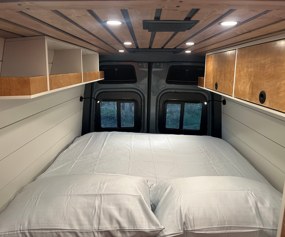 Cozy RV rental interior featuring a comfortable bed, built-in storage, stylish ceiling, and scenic rear windows. — photo 2