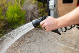 A hand uses a spray nozzle to rinse outside an RV rental, highlighting easy outdoor clean-up for camping or van life.
