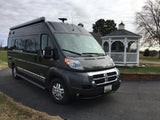 A sleek, dark grey Winnebago Travato van RV, ideal for your next rv rental and road trip, parked by a white gazebo.