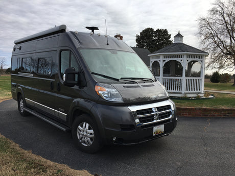 A sleek, dark grey Winnebago Travato van RV, ideal for your next rv rental and road trip, parked by a white gazebo.
