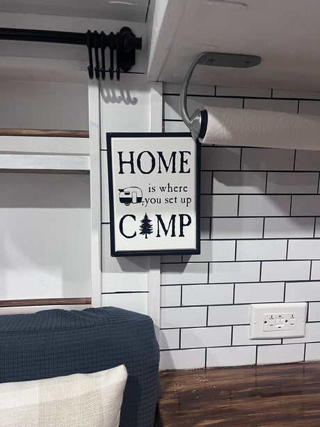 Cozy RV rental kitchen featuring a "HOME is where you set up CAMP" sign, paper towel holder, and tiled backsplash.