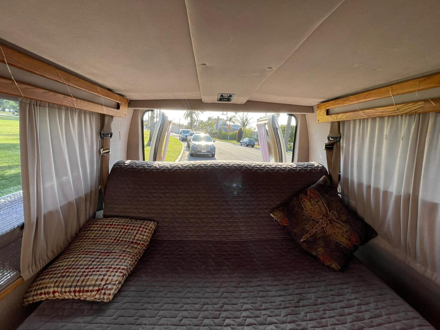 RV rental's cozy interior: a comfortable bed offers a view out open doors to a sunny, tree-lined street.